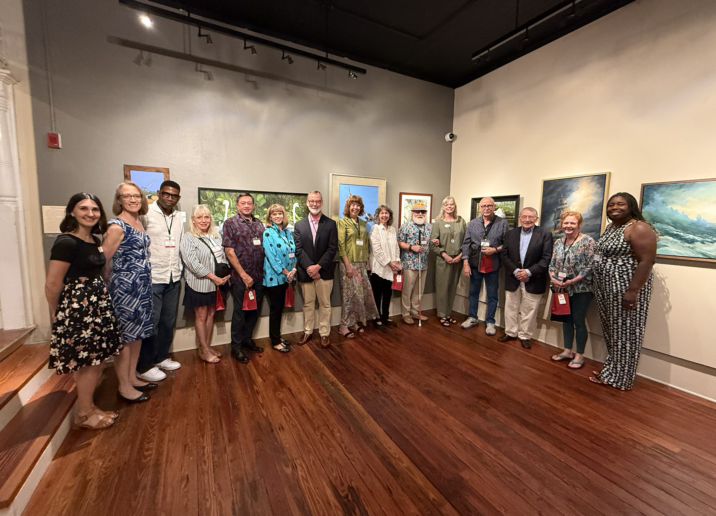 Group of adults posing for a photo in an art gallery, standing in front of paintings along the wall.