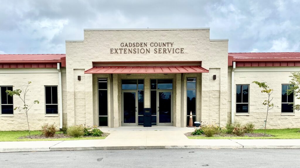 Front view of the Gadsden County Extension Service building, featuring a red metal roof, beige exterior, and symmetrical windows.