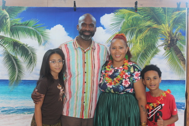 Family of four in colorful outfits pose in front of a tropical beach backdrop.