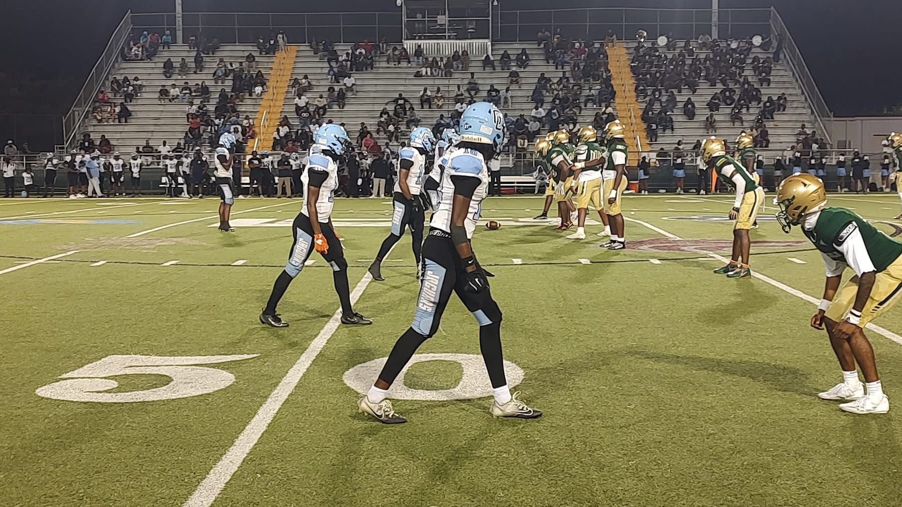 Football teams line up at the 50-yard line under stadium lights during a night game.