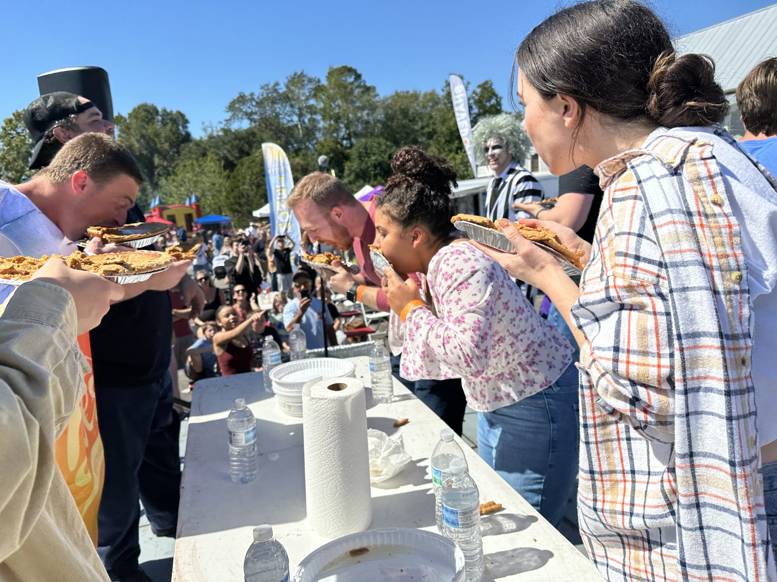 Contestants participate in a pie-eating competition outdoors before a crowd.
