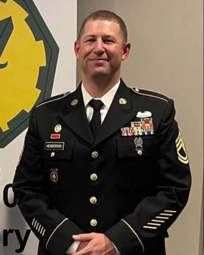 U.S. Army sergeant in formal dress uniform standing indoors, wearing service ribbons and insignia, smiling toward the camera.