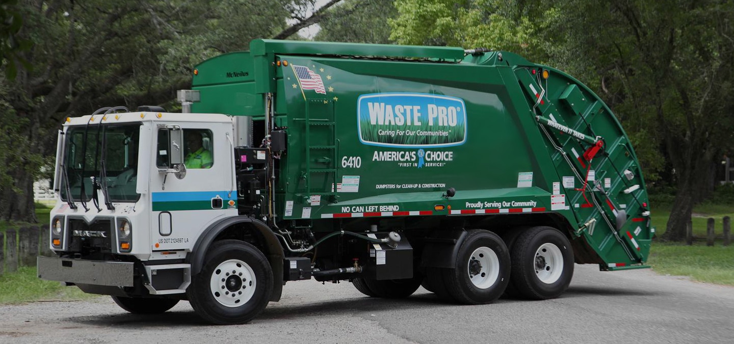 A green Waste Pro garbage truck is parked on a residential street lined with trees.