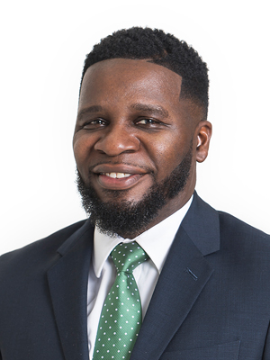 Portrait of Ronterious Green in a suit and green tie, smiling against a light gray background.