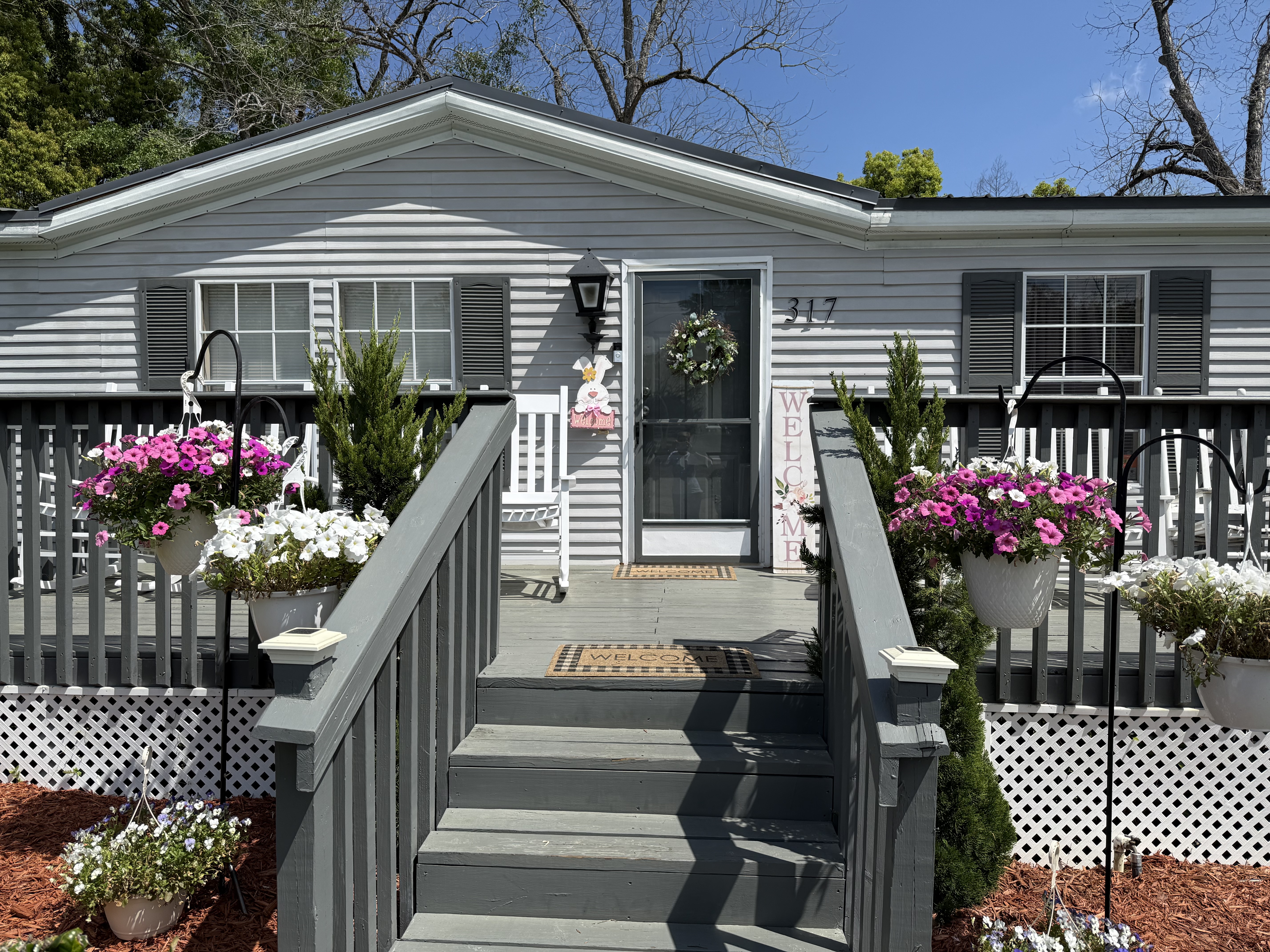 Front of a gray house at 317 Gay Street with a small porch and steps, decorated with hanging baskets and potted flowers, recognized as Havana Garden Club Residential Yard of the Month.