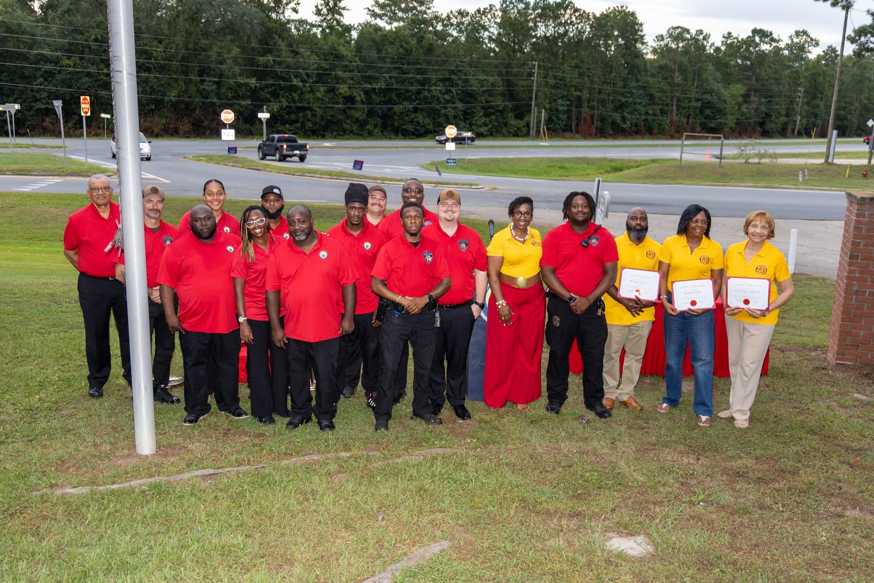 A large group pose of city staff, officials, and committee members wearing red and yellow shirts standing outdoors.